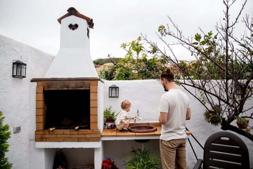 A man and a child standing near an out door brick piza oven