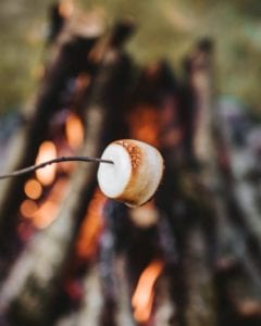 Close up of marshmallow on a stick being grilled over a firepit.