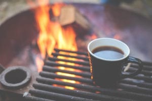 A cup of coffee with a fire pit in the background.