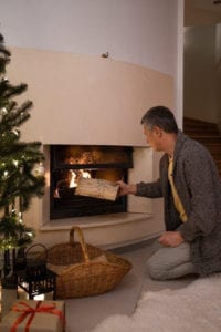 A man adding firewood to the fireplace.