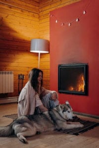 A women snuggling with her dog on a hearth rug in front of their fireplace. 