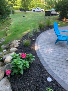 flowering landscape around a stone fire pit with blue patio chair