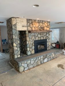 This is a picture of a natural stone fireplace building build in someone's home in Maine