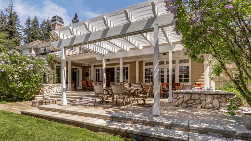 Backyard pergola with stone foundation, comfortable outdoor furniture, and coordinated decor featuring elegant white columns, professional landscaping and flowering lilacs