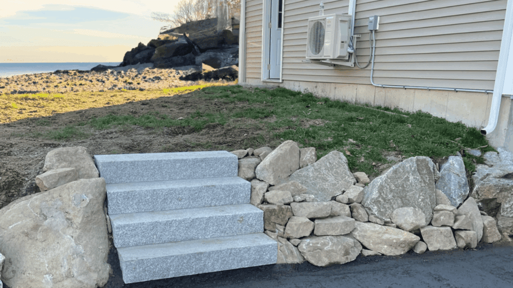 Beachfront granite steps with natural boulder retaining wall, coastal home entrance with ocean view and rocky shoreline, featuring minimalist landscape design