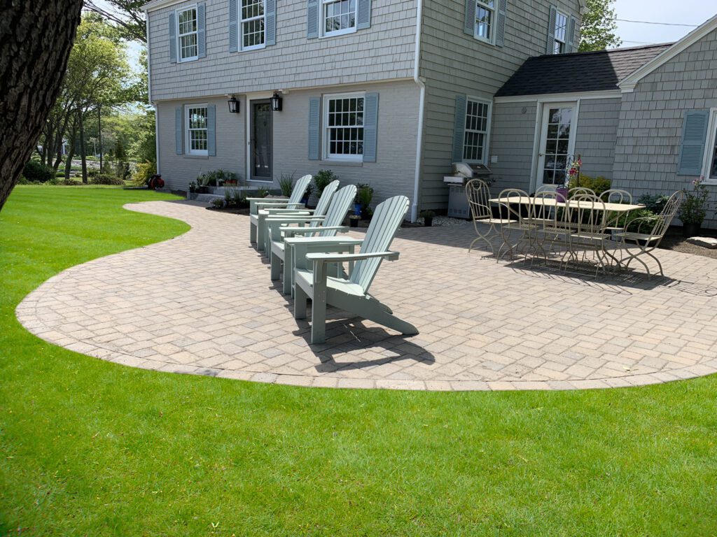 Classic New England home with curved paver patio, mint green Adirondack chairs, and bistro dining set, professionally designed front yard landscaping with Colonial style architecture