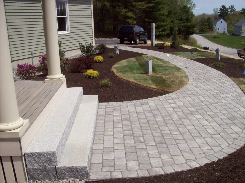 Curved paver walkway with granite light posts leading to a front entry with granite steps in Southern Maine