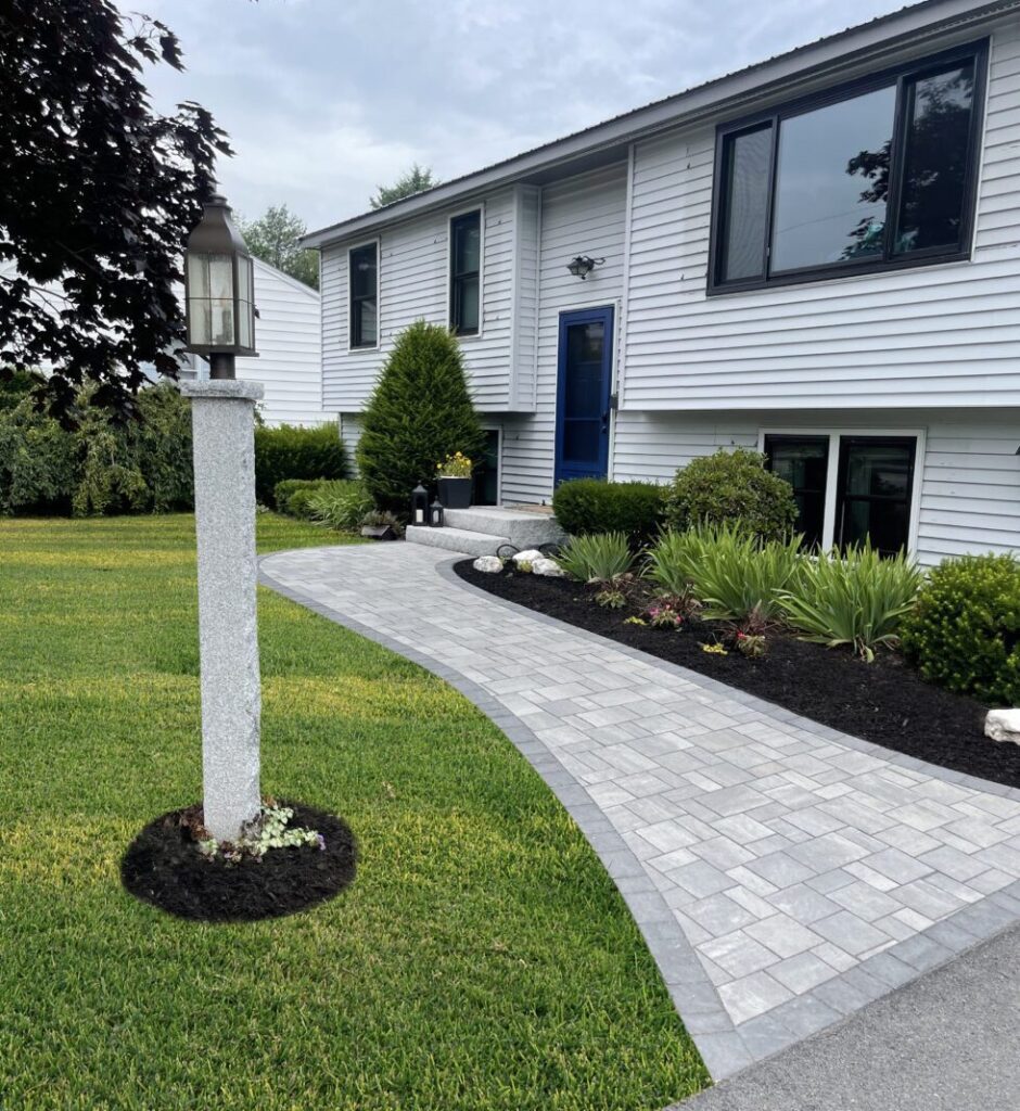 Curved gray paver walkway with granite light post leading to a home with a blue front door in Southern Maine
