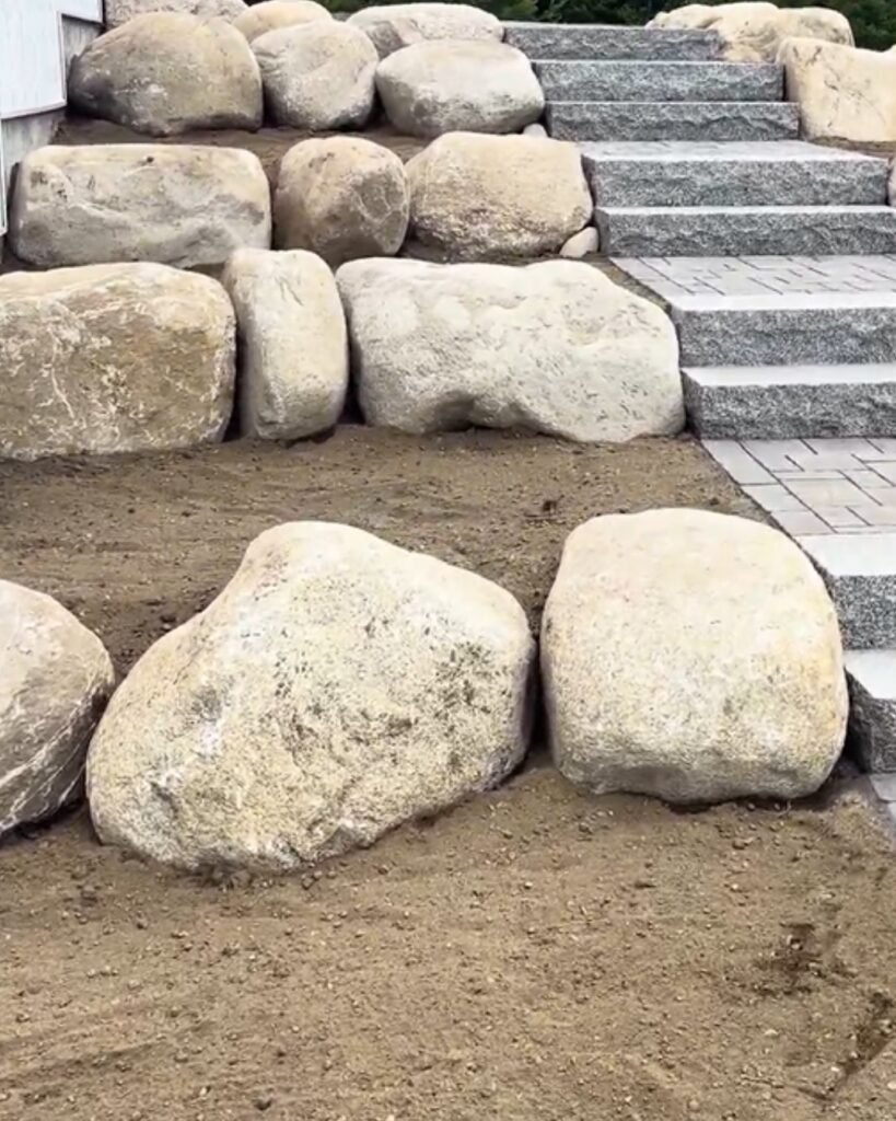 lose-up of natural fieldstone boulders bordering rough-cut granite steps and a paver landing on a hillside hardscape project in Scarborough, Maine