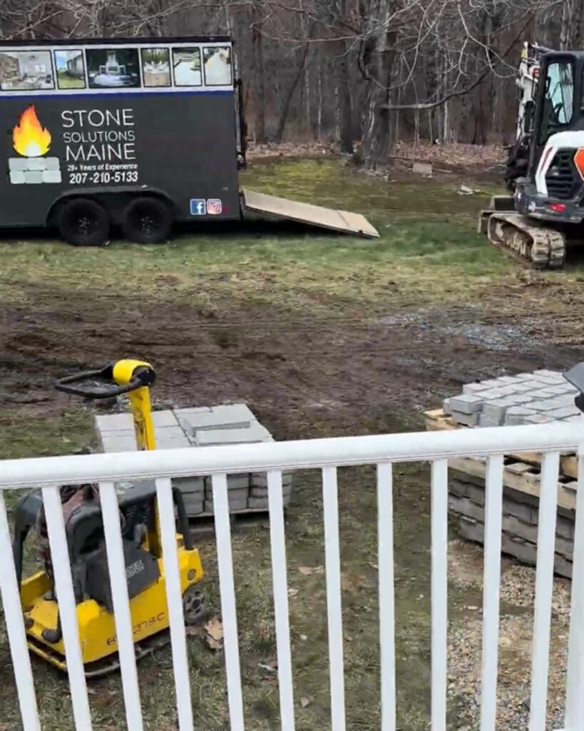 Stone Solutions Maine trailer, excavator, and Genest paver pallets staged at a Durham, Maine patio jobsite