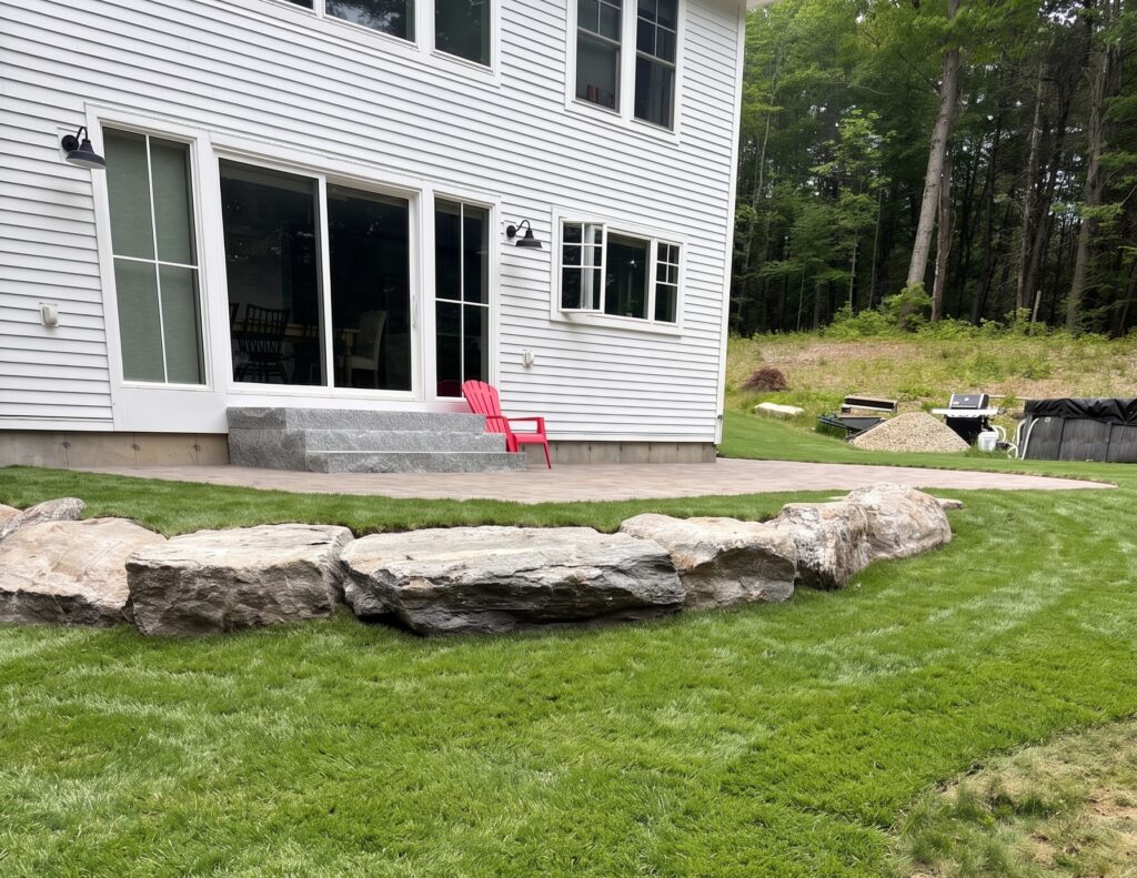 Boulder landscaping and grading around a paver patio in a Pownal, Maine backyard