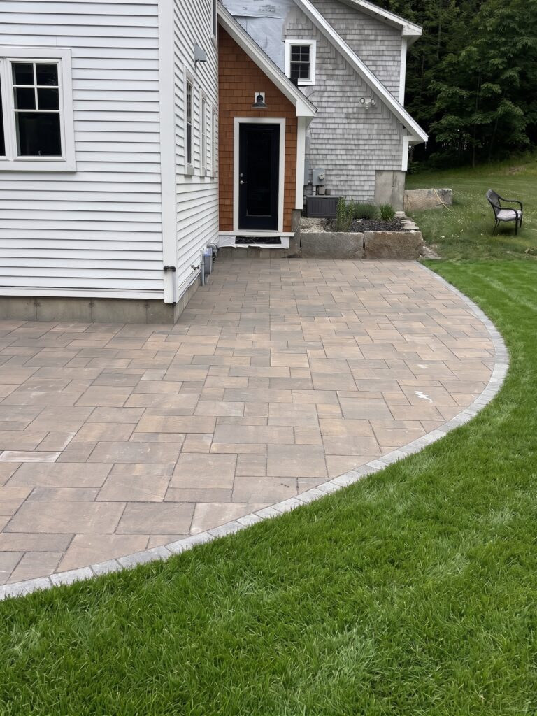 Curved paver patio with granite planter boxes near a home entrance in Pownal, Maine